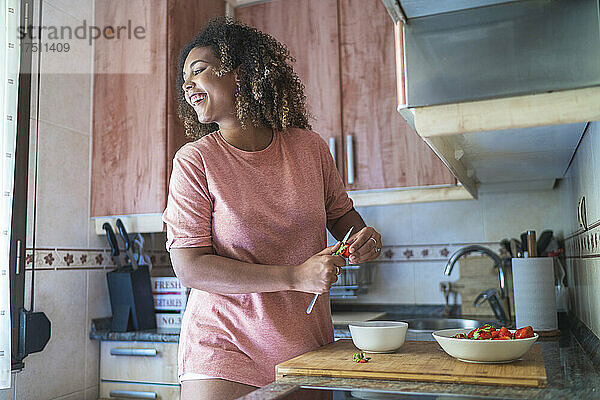 Fröhliche junge Frau schaut weg  während sie zu Hause auf der Küchentheke Erdbeeren hackt