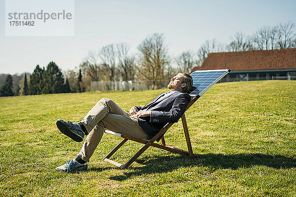 Geschäftsmann entspannt sich an sonnigen Tagen auf einem Stuhl mit Solarpanel im Park