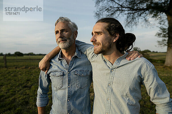 Vater und erwachsener Sohn umarmen sich auf einer Wiese auf dem Land