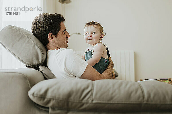 Vater hält süße kleine Tochter in der Hand  während er sich zu Hause auf dem Sofa entspannt