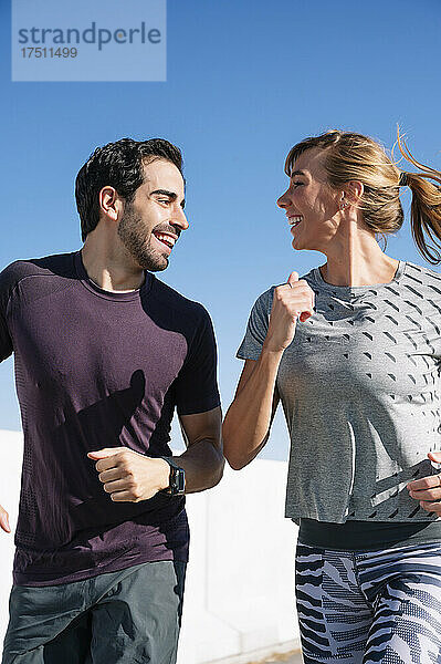 Lächelndes Paar  das sich an einem sonnigen Tag beim Laufen gegen den klaren blauen Himmel anschaut