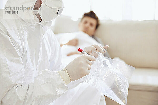 Nahaufnahme eines Arztes  der eine medizinische Probe in einer Plastiktüte hält  während der Patient auf dem Sofa ruht