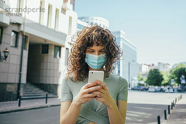 Frau trägt Schutzmaske und benutzt Smartphone in der Stadt