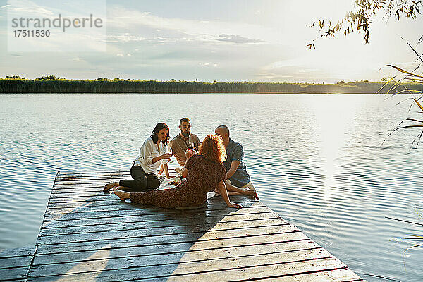 Freunde machen bei Sonnenuntergang ein Picknick am Steg an einem See