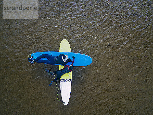 Aerial view of two surfers lying on surfboards in brown water of Barents Sea