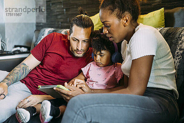 Eltern mit ihrer Tochter nutzen ein digitales Tablet  während sie sich zu Hause auf dem Sofa entspannen