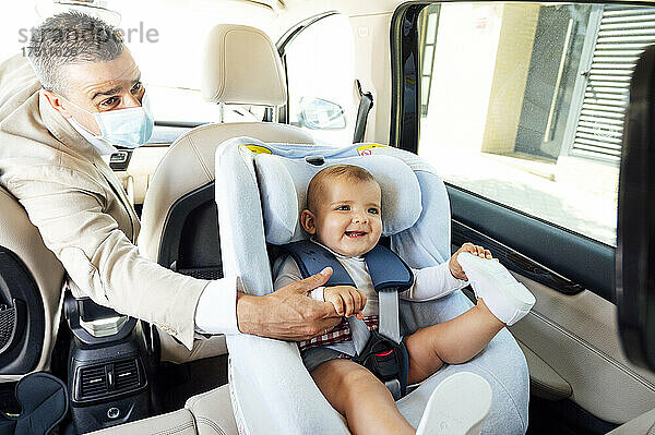 Vater trägt Schutzmaske  kleiner Junge sitzt im Kindersitz in einem Auto