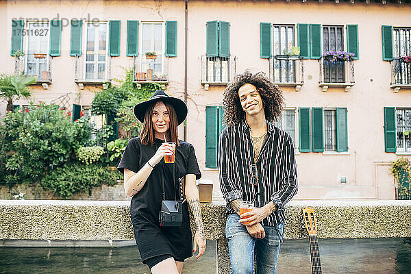 Lächelndes Paar hält Getränke in der Hand und steht vor einem Gebäude in der Stadt