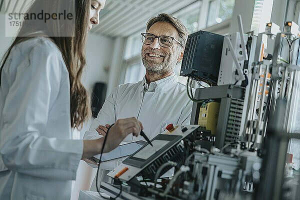 Lächelnder Mann blickt Kollegin an  die im Labor Maschinen bedient