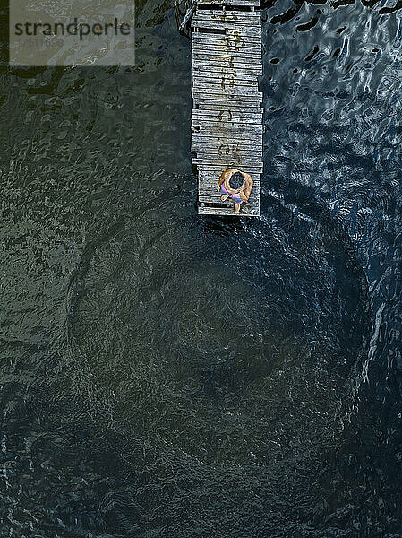 Luftaufnahme eines Mannes  der am Rand eines Stegs am Seeufer steht