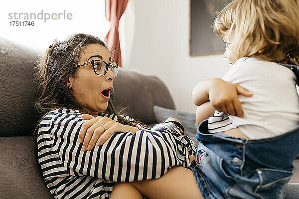 Glückliche Mutter spielt mit ihrer Tochter  während sie zu Hause auf dem Sofa sitzt