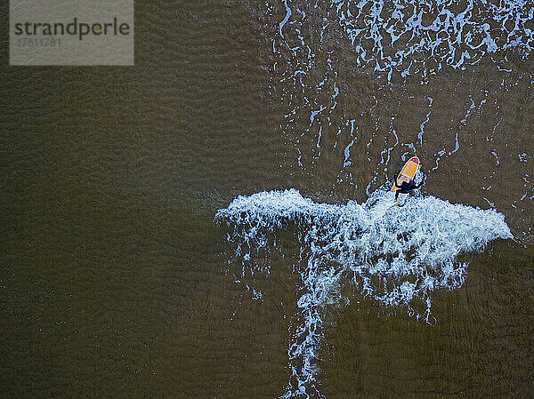 Luftaufnahme eines Mannes  der im braunen Wasser der Barentssee surft