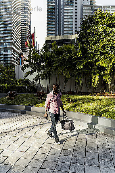 Afro-junger Mann mit Tasche läuft auf Fußweg in Miami City  Florida  USA
