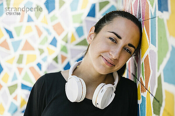 Porträt einer Frau mit weißem Kopfhörer vor einer bunten Wand
