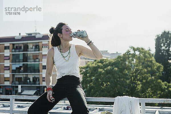 Frau trinkt Wasser  während sie draußen auf dem Geländer sitzt