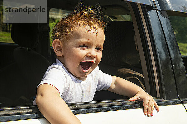 Lächelnder kleiner Junge  der aus dem Autofenster schaut