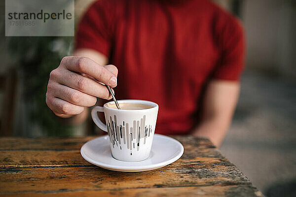 Nahaufnahme der Hand eines Mannes  der Kaffee rührt  während er im Straßencafé sitzt