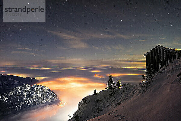 Abgeschiedene Berghütte in der Abenddämmerung mit beleuchtetem Tal im Hintergrund