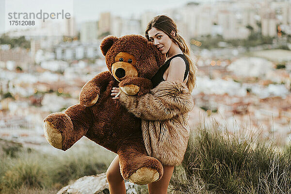 Junge Frau umarmt Teddybär  während die Stadt im Hintergrund liegt