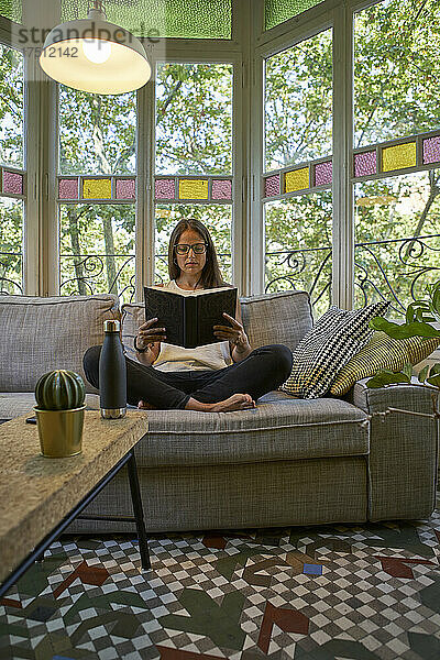 Frau liest ein Buch  während sie auf dem Sofa im Wohnzimmer sitzt