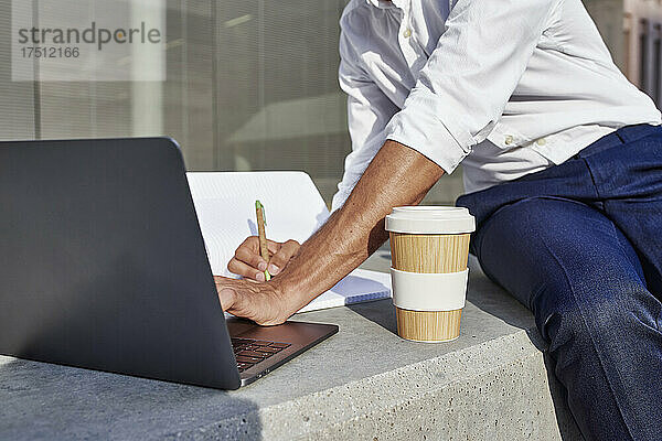 Geschäftsmann mit Laptop und Einwegbecher schreibt  während er in der Stadt sitzt