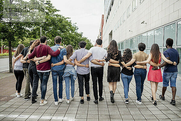 Weibliche und männliche Freunde gehen mit Armen auf dem Fußweg in der Stadt spazieren