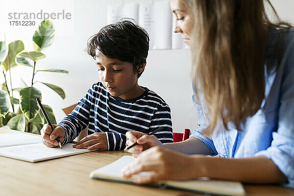 Nahaufnahme einer Nachhilfelehrerin  die einen Jungen beobachtet  der seine Hausaufgaben auf dem Tisch schreibt