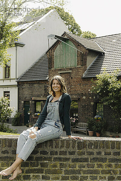 Porträt einer lächelnden jungen Frau  die auf einer Ziegelmauer in einem Bauernhaus sitzt
