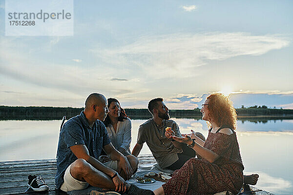 Freunde machen bei Sonnenuntergang ein Picknick am Steg an einem See