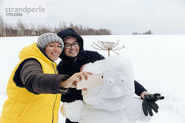 Smiling couple taking selfie with snowman
