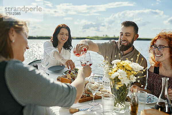 Freunde essen an einem See zu Abend und trinken Wein