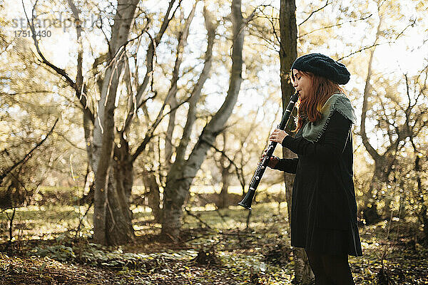 Junge Musikerin übt das Klarinettenspiel  während sie im Herbst im Wald steht