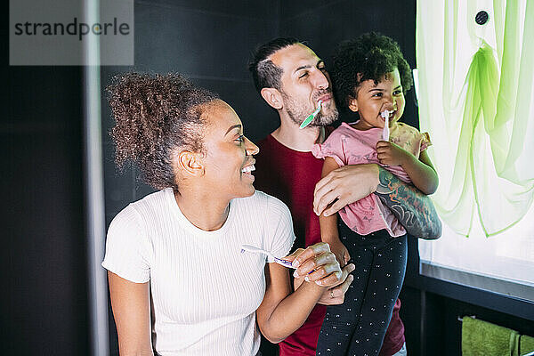 Glückliche Eltern mit ihrer Tochter beim Zähneputzen im Badezimmer zu Hause