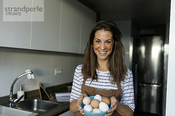 Lächelnde junge Frau hält Eier in der heimischen Küche