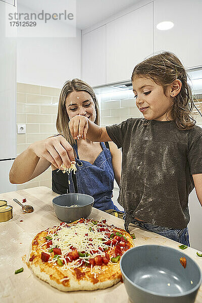 Mutter und Tochter werfen Käse auf Pizzateig in der Küche