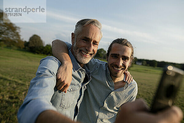 Glücklicher Vater und erwachsener Sohn machen ein Selfie auf einer Wiese auf dem Land