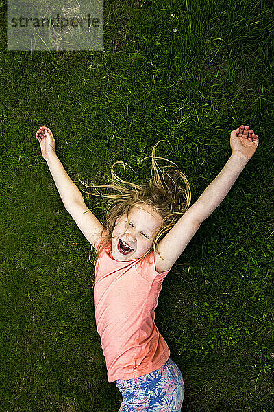 Fröhliches Mädchen liegt mit geschlossenen Augen im Gras