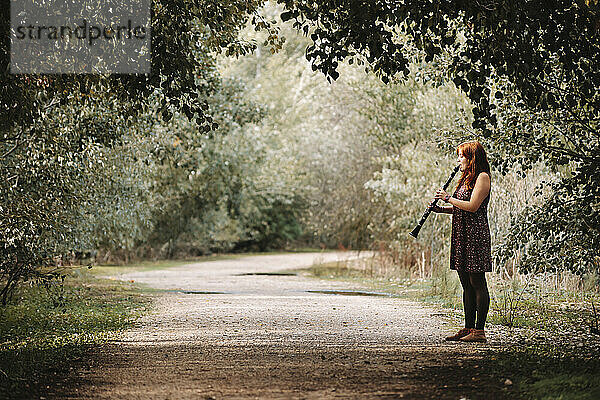Junge Frau übt Klarinette  während sie auf einem Fußweg im Wald steht