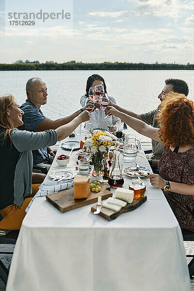 Freunde essen an einem See zu Abend und stoßen mit Weingläsern an