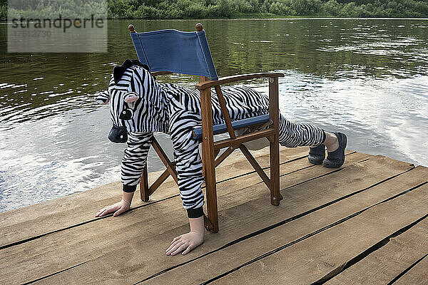 Junge im Zebrakostüm trainiert auf einem Stuhl über der Promenade
