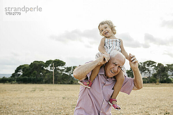 Glücklicher Großvater trägt seine Enkelin auf den Schultern  während er vor dem Himmel steht