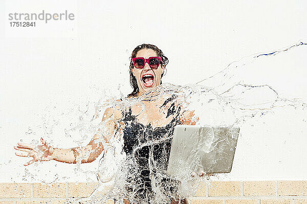 Frau mit Laptop schreit  während Wasser auf sie gegen die Wand spritzt