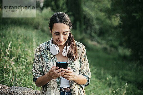Lächelnde Frau  die im Park Nachrichten über ihr Smartphone sendet