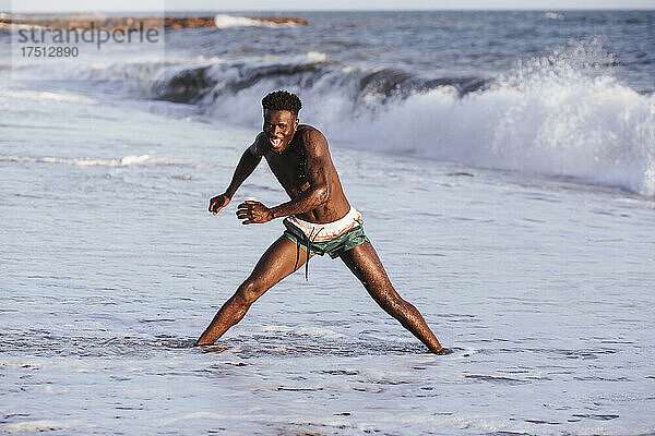 Fröhlicher junger Mann ohne Hemd trainiert  während er im Meer steht