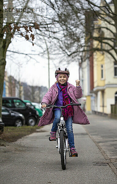 Lächelndes Mädchen mit Helm  das auf der Straße in der Stadt Fahrrad fährt