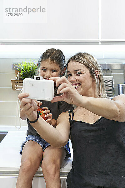 Glückliche Mutter macht ein Selfie mit ihrer Tochter  die zu Hause auf der Küchentheke sitzt