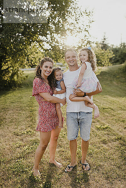 Porträt glücklicher Eltern mit zwei Töchtern  die auf einer Wiese stehen