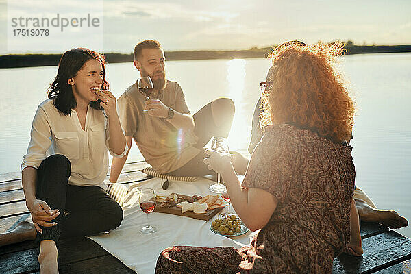 Freunde machen bei Sonnenuntergang ein Picknick am Steg an einem See