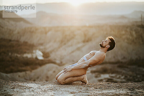 Nackter Mann mittleren Alters kniet bei Sonnenuntergang an Land in der Wüste