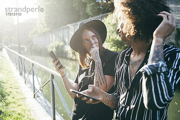 Paar hält Mobiltelefone in der Hand und schaut einander an  während es im Park steht